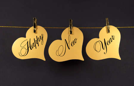 Happy New Year message greeting text on gold hearts hanging from pegs on a line against a blackの写真素材