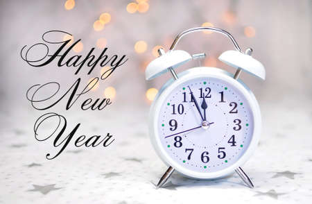Happy New Year message with white retro clock showing five to midnight on white starry with bokeh...