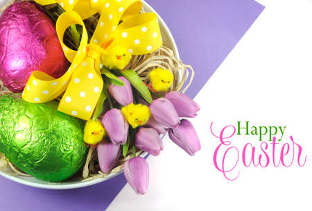 Happy Easter basket of colorful pink and green foil wrapped eggs and pink purple tulips with chicks...