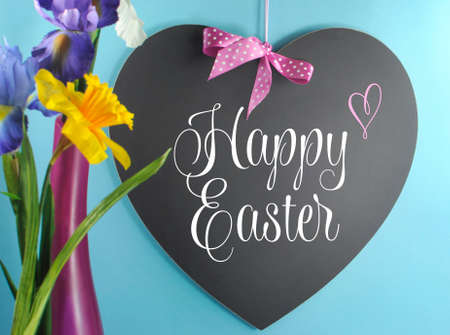Happy Easter greeting on heart shape blackboard or copy space with spring flowers in pink vase on blue background.の写真素材