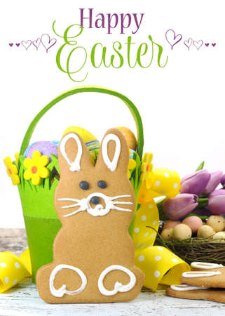 Happy Easter yellow and lime green theme gingerbread bunny cookie with basket, tulips, and candy birds eggs in nest on shabby chic wood and white background の写真素材