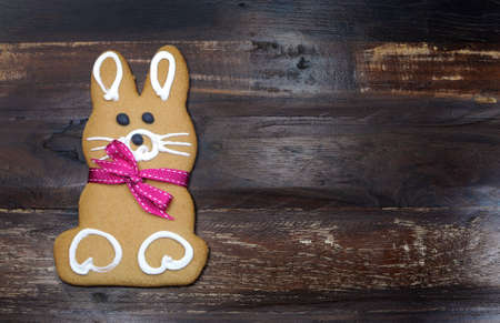 Happy Easter bunny rabbit gingerbread cookie with pink ribbon on dark recycled vintage retro wood...