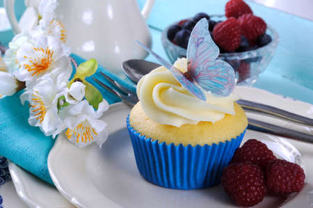 Close up of delicious cupcake with butterfly wafer decoration on vintage aqua blue tray setting with berries and cream.の写真素材