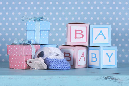 Baby nursery bootie, dummy pacifier and baby letters pink and blue gift boxes against a vintage aqua blue table and polka dot background for baby shower or newborn girl greeting card の写真素材