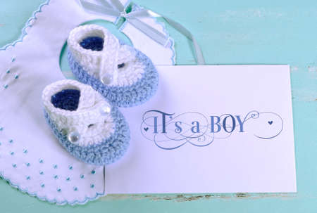 Baby boy nursery blue and white wool booties, bib and card with Its A Boy sample text, on aqua vintage shabby chic background for baby shower or newborn girl greeting card の写真素材
