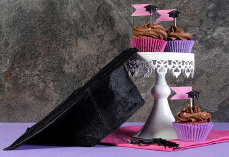 Graduation day pink and purple party chocolate cupcakes on white vintage white stand with graduation cap の写真素材