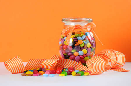 Candy in glass jar with orange and white stripe ribbon for Halloween or party favors.の写真素材