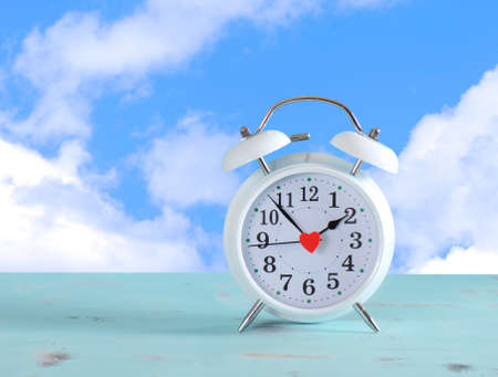 Daylight savings time white clock on a vintage aqua blue wood table against a sky with clouds background.の写真素材
