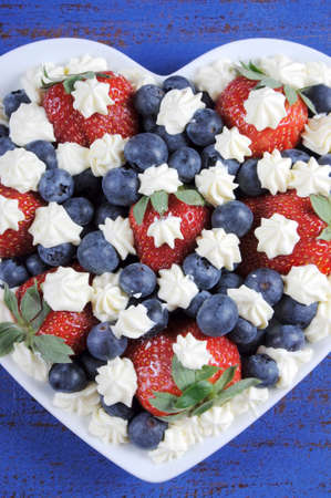 Patriotic red, white and blue berries with fresh whipped cream stars in white heart shape flag on rustic dark blue wood background. Vertical elevated aerial view.の写真素材