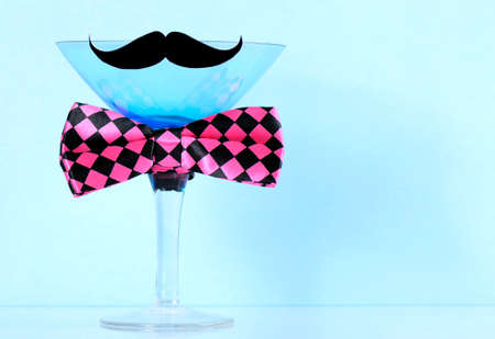 November fundraising for mens health awareness charity with mustache and bow tie on blue martini cocktail glass on blue background, with copy space.の写真素材