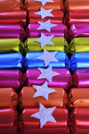 Row of shiny festive Christmas cracker bon bons in bright cheerful red, pink, orange, blue and green colors. Vertical.の写真素材