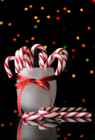 Festive Christmas candy canes on reflective table with bokeh lights on black background. Vertical.の写真素材