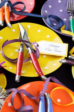 Bright and colorful Happy New Year party dinner table with red, yellow, orange, blue, green, and...