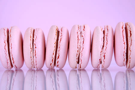 Row of pink macaron cookies lined up on reflective table against a pink background.の写真素材