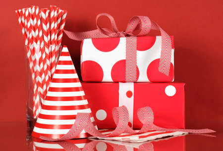 Red and white theme happy birthday party with stack of gifts, party hat and straws on red background.の写真素材