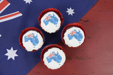 Happy Australia Day January 26 party food with red velvet cupcakes and Australian maps rice paper toppers on dark red and blue vintage rustic recycled wood background.の写真素材