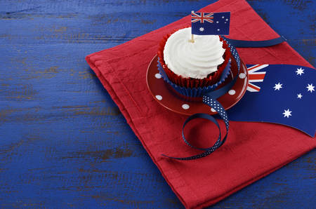 Happy Australia Day, January 26, theme table setting with red, white and blue cupcake on red polka dot plate and Australian flag decoration on dark blue wood background.の写真素材