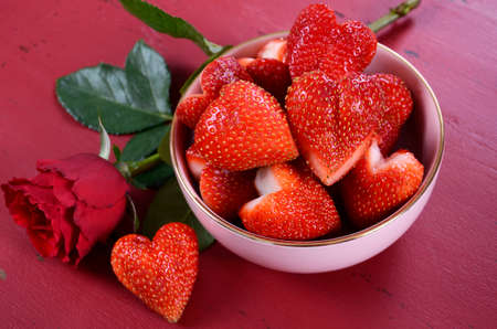 Happy Valentines Day bowl of luscious heart shape red strawberries on a red vintage wood background.の写真素材