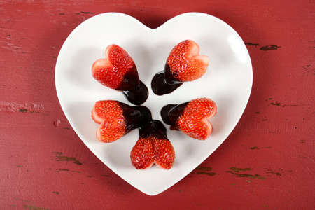 Happy Valentines Day chocolate dipped heart shaped strawberries on heart shape white plate on red vintage wood background, overhead view.の写真素材