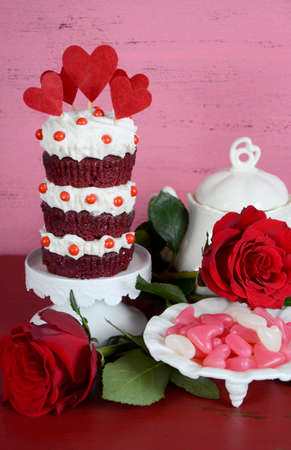 Vintage style triple layer red velvet cupcake on white cake stand with roses and candy against a...
