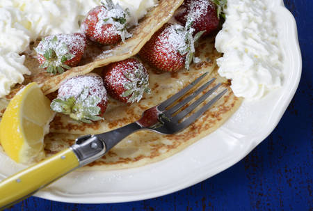 Shrove Pancake Tuesday pancakes with strawberries and cream on dark blue vintage shabby chic table,...