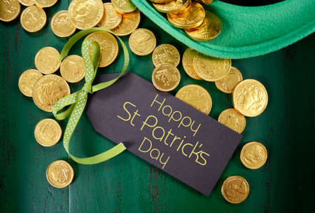 Happy St Patricks Day leprechaun hat with gold chocolate coins on vintage style green wood...