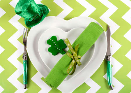 Happy St Patricks Day table place setting with heart shape plates, shamrock cookie and leprechaun...