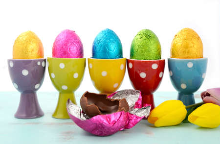 Happy Easter row of chocolate eggs wrapped in bright color foil in red, yellow, blue, green and...
