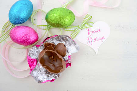 Happy Easter pink, green, and blue foil wrapped chocolate eggs on shabby chic vintage style white wood background.の写真素材