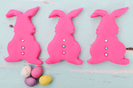 Happy Easter pink confectionary sugar fondant cookie bunnies on pale aqua blue shabby chic vintage style wood table.の写真素材