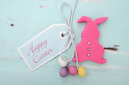Happy Easter pink confectionary sugar fondant cookie bunny with greeting tag on pale aqua blue...
