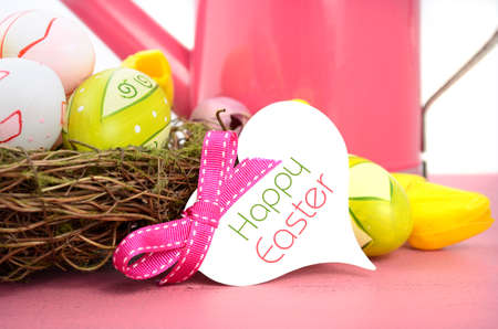 Happy Easter Spring theme pink watering can with easter eggs and eggs, nest and flowers on pink wood table against a white background, closeup with gift tag and sample tag.の写真素材