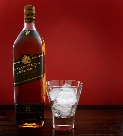 ADELAIDE, SOUTH AUSTRALIA â FEBRUARY 23, 2015: Photo of a bottle of Johnnie Walker Green Label Pure Malt Scotch Whisky with ice in glass on a dark wood table against a red background, now discontinued and considered rare.のeditorial素材