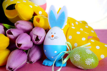 Happy Easter egg hunt baskets with tulip flowers and eggs with bunny ears and faces on a pink wood table.の写真素材