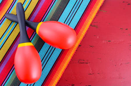 Happy Cinco de Mayo background with red and yellow maracas on Mexican style fabric and distressed red wood table.の写真素材