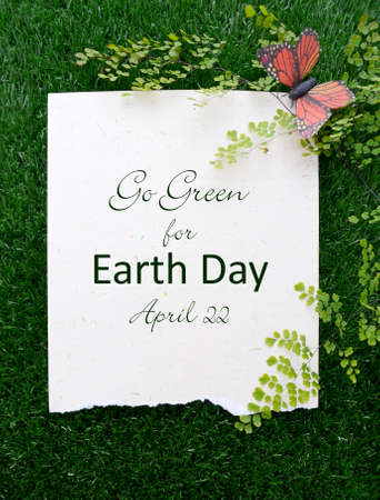 Earth Day, April 22, Concept with recycled paper in grass with fern and butterfly and text.