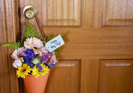 Happy May Day traditional gift of Spring flowers in orange cone hanging from door handle on wooden door.の写真素材