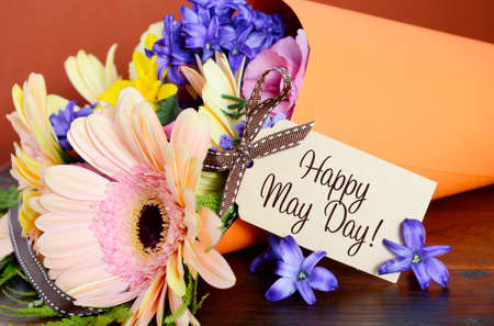 Happy May Day traditional gift of Spring Flowers in orange paper cone on dark wood table.の写真素材