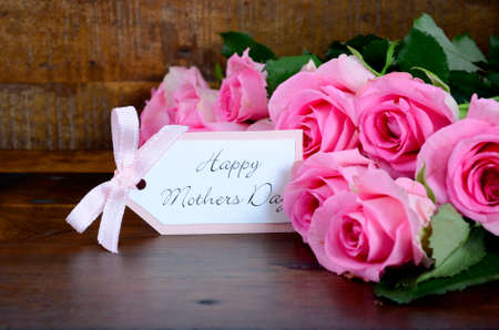 Happy Mothers Day fresh pink roses on dark wood distressed table and background, with gift tag.の写真素材