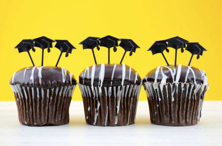 Happy Graduation Day party chocolate cupcakes with graduation cap hat topper decorations, in yellow, black and white party theme.の写真素材