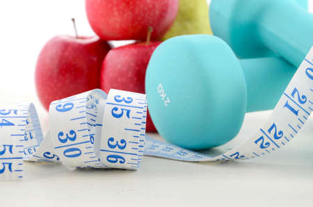 Health and fitness concept with blue dumbbells, tape measure and  fresh fruit on white distressed wood table background, close up.の写真素材