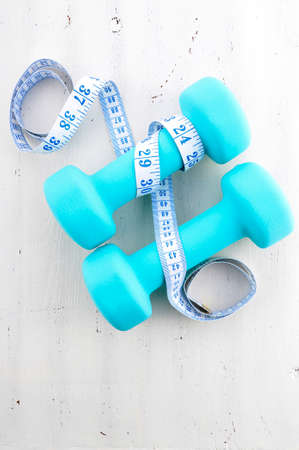 Health and fitness concept with pale blue dumbbells and tape measure on white distressed wood table background.の写真素材