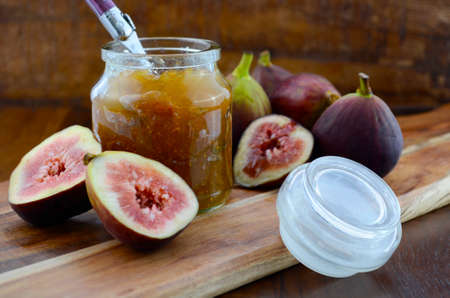 Fresh figs on wooden cutting chopping board with jar of fig jelly preserve on dark wood rustic table background.の写真素材
