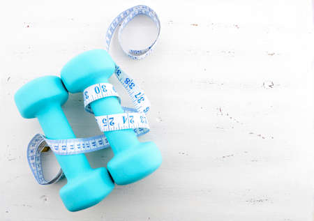 Health and fitness concept with pale blue dumbbells and tape measure on white distressed wood table background.の写真素材