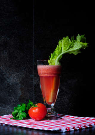 Healthy freshly made tomato and celery vegetable juice on vintage style red check napkin against black slate kitchen bench top.の写真素材