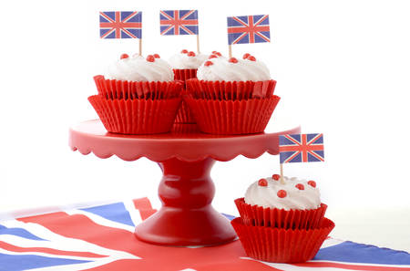 Red white and blue theme cupcakes on red cake stand with UK Union Jack flags on white wood table for Queens Birthday and Great Britain party food.の写真素材