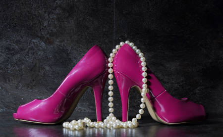 Glamorous pair of ladies pink high heels with long strand of white pears against a dramatic black slate background still life.の写真素材