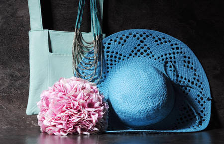 Ladies vintage retro style apparel with aqua blue sun hat, shoulder bag and necklace with bunch of pink hydrangea flowers against a dramatic black slate background.の写真素材