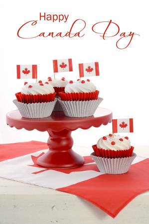Happy Canada Day celebration cupcakes with red and white maple leaf flag on red cake stand against a white background, vertical with sample text.の写真素材