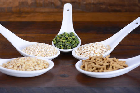 Healthy High Fiber Prebiotic Grains in serving spoons, including wheat bran cereal, oat flakes, dried legume peas, oat bran and pearl barley, on rustic dark wood table.の写真素材